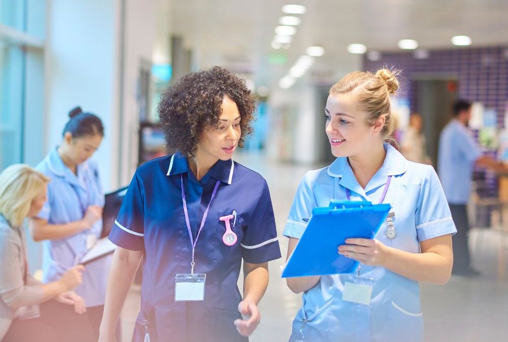 Two nurses look and discuss patient's medical record while walking in a hospital setting